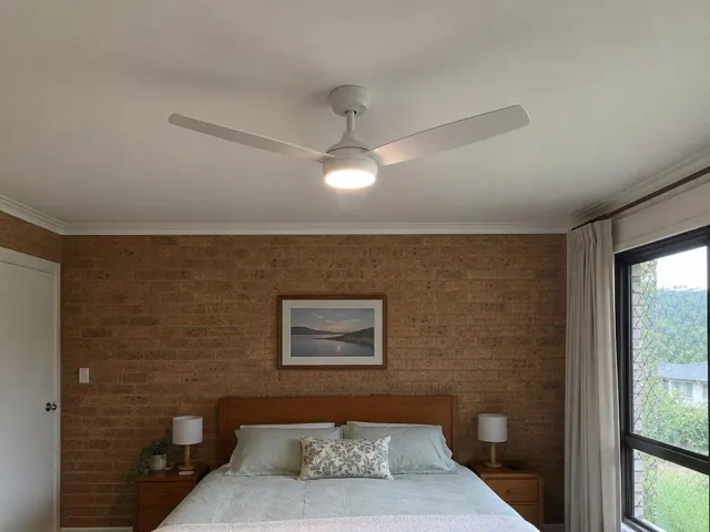Ceiling fan centered above a bed in a brick bedroom with window and curtains in Wangi Wangi